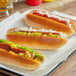 Three Brioche Gourmet plant-based hot dogs on a tray with condiments.