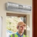 A man wearing a yellow vest and hard hat standing next to a door with a Boltic stainless steel air curtain installed.