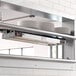 A ServIt double strip warmer mounted on a wall above a plate rack with plates on it.