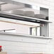 A ServIt strip warmer on a stainless steel shelf above plates in a professional kitchen.