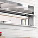 A stainless steel shelf with a ServIt Strip Warmer above plates on a counter in a professional kitchen.