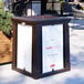 A brown Suncast outdoor waste container with open top lid and white sign frames.