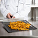 A person in a chef's coat cutting french fries on a black Essentialware mesh screen.
