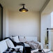 A matte black Globe outdoor flush mount light with a metal shade above a couch with pillows and blankets.