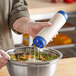 A hand using a Vollrath Traex squeeze bottle to pour dressing onto a salad.