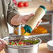 A person using a Vollrath Traex clear squeeze bottle to pour dressing on a bowl of salad.