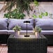 A black Globe battery-powered LED table lamp on an outdoor patio table next to a potted plant.