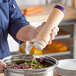 A person pouring sauce from a Vollrath Traex FIFO squeeze bottle into a bowl of salad.