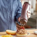 A person using a Vollrath Traex clear squeeze dispenser to pour ketchup onto a plate of food.