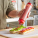 A person pouring sauce onto a sandwich using a Vollrath Traex squeeze bottle.