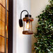 A Globe matte black outdoor wall sconce with faux wood accent and cylindrical glass shade on a wall.