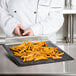 A chef uses an Essentialware loose weave mesh screen to cook french fries on a black mesh tray.