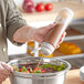 A person pouring brown sauce from a Vollrath Traex squeeze bottle into a bowl of salad.