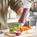 A person pouring a brown sauce into a sandwich using a Vollrath Traex clear squeeze bottle.