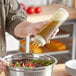 A hand using a Vollrath Traex squeeze dispenser to pour oil onto a bowl of salad.