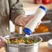 A hand using a Vollrath Traex clear squeeze bottle with blue tip to pour dressing on a salad.