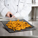 A chef holding a pile of french fries on a Essentialware loose weave mesh screen.