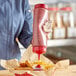 A gloved hand using a Vollrath Traex squeeze bottle to pour ketchup on french fries.