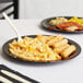 A plate of macaroni and cheese on a Cambro black polycarbonate narrow rim plate with a fork.