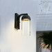 A Globe matte black wall sconce with a glass shade on a white wall.
