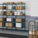 Blue metal Lavex Pro wire shelving with white rectangular boxes on the shelves.