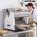 A person in a white coat and gloves using an Estella countertop bread slicer to slice bread.