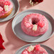 A pink donut with pink frosting and Albanese Lovestruck Gummi Bears on top.