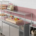 An Avantco stainless steel single deck overshelf on a counter in a kitchen with shelves of food.