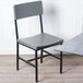 A BFM Seating Memphis grey steel side chair with black legs and wooden seat and back.