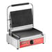 An Avantco commercial panini grill with grooved plates on a counter. The grill has a red and black handle.