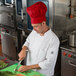 A man in a red Intedge chef hat cutting vegetables on a cutting board.