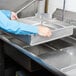 A person using an Advance Tabco pre-rinse basket over a sink.