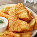 A plate of fried fish and fries with a lemon wedge and white sauce.