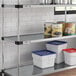 A Regency galvanized steel shelf with white, blue, and red plastic containers on it.