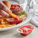 A hand dipping a french fries into a Heinz Dip & Squeeze Ketchup packet on a table with a burger.