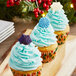 Cupcakes with blue frosting and star decorations on a table with white plates.