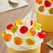 A yellow cupcake with whipped cream and a gummy apple on top.