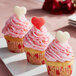 Cupcakes with pink frosting and Albanese sour gummi hearts on top on a plate in a bakery display.