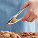 A person using a Vollrath lobster and nut cracker to crack a nut over a bowl of nuts.