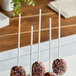 A group of chocolate covered cake pops on white Wilton treat sticks with sprinkles.