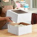 A woman holding a white Wilton bakery box with flowers inside.