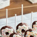 A white frosted doughnut on a white paper treat stick with sprinkles.