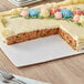 A Wilton white rectangular cake board with a carrot cake with frosting and flowers on it on a table with a fork and napkin.
