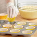 A person wearing gloves placing a yellow Wilton cupcake wrapper with colorful polka dots into a muffin tin.