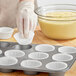 A person putting a Wilton white cupcake wrapper into a muffin tin.