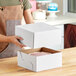 A woman holding a white Wilton cake box with a cake inside.