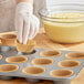 A gloved hand putting a Wilton Kraft unbleached cupcake wrapper into a muffin tin.