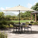 A table and chairs under a white Lancaster Table & Seating umbrella with a black pole.