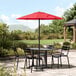 A black Lancaster Table & Seating table and chairs on a stone patio with a red umbrella.