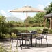 A Lancaster Table & Seating woodgrain aluminum umbrella over a table with chairs on a patio.